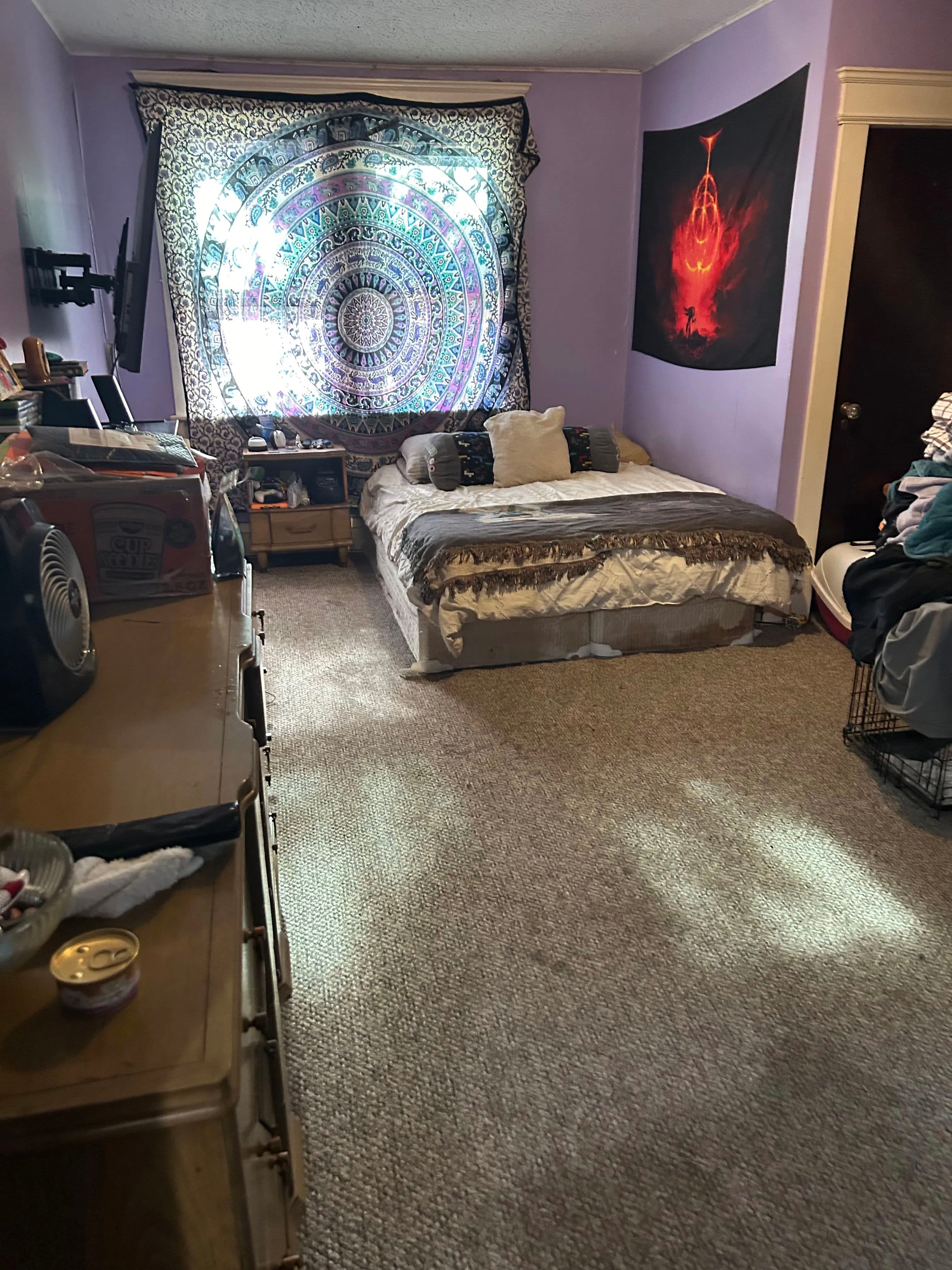 Cozy bedroom with a purple wall, patterned tapestry, and a neatly made bed.